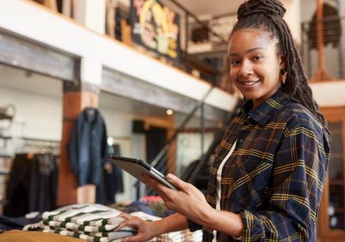 Portrait Of Female Owner Of Fashion Store Using Digital Tablet To Check Stock In Clothing Store